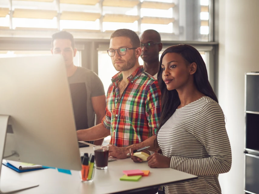 Four diverse workers standing next to computer.