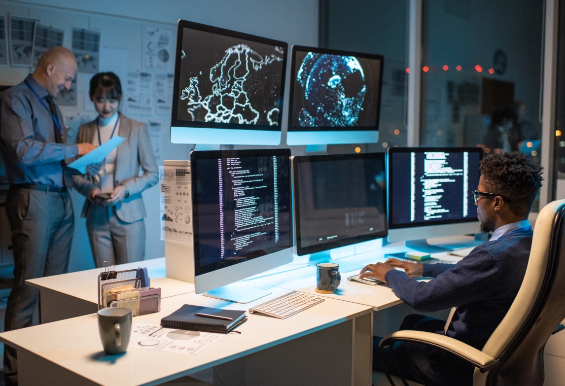 A man works at a desk with 5 monitors in front of him.