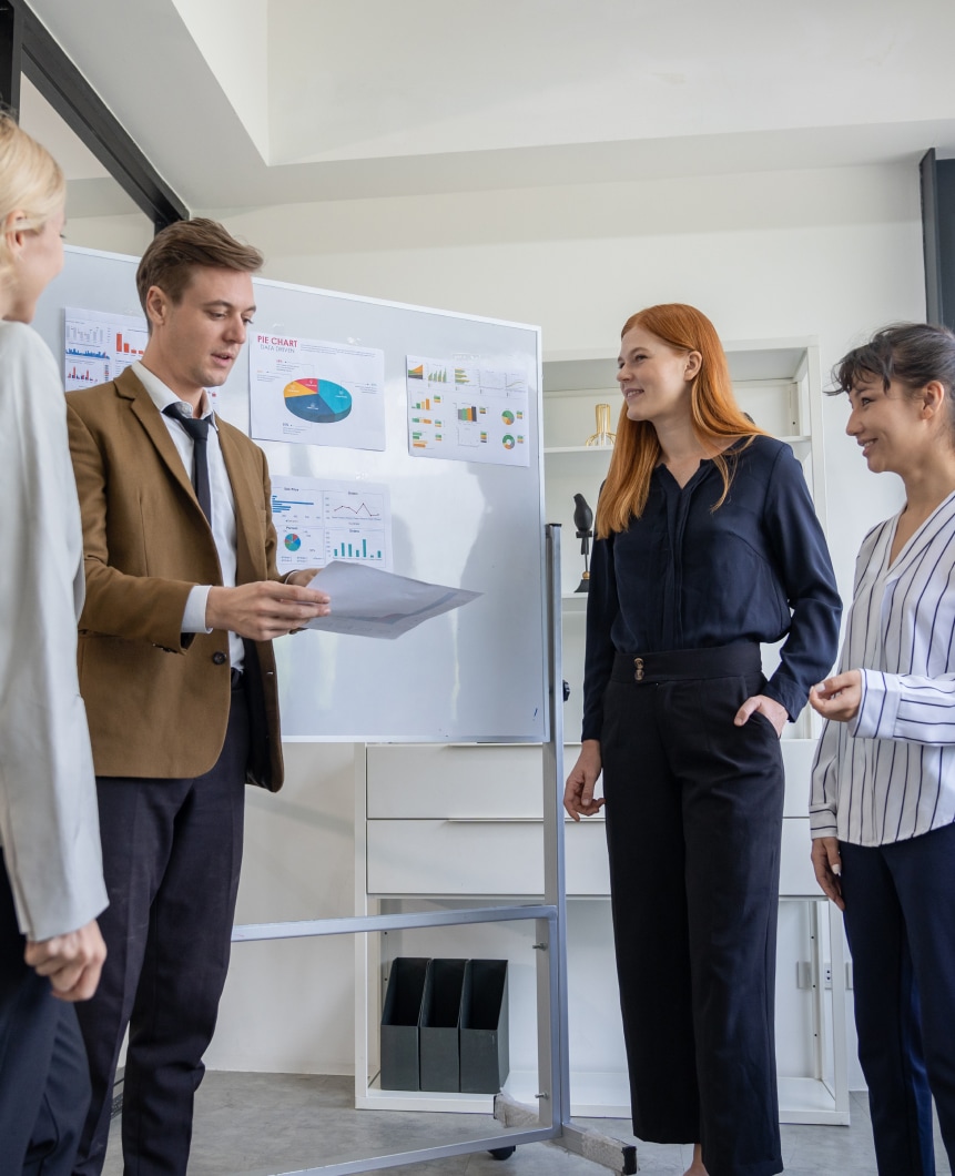 Four people are discussing in front of a white board.