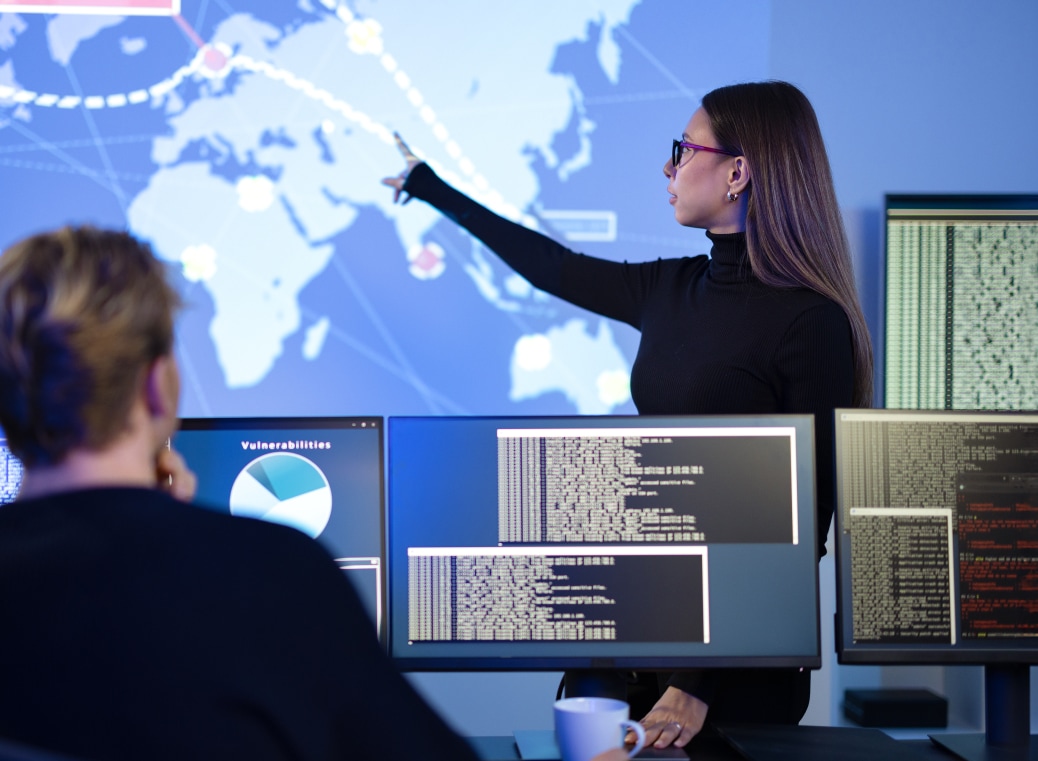 Аman is sitting at a computer and in front of him is a girl pointing to a world map.