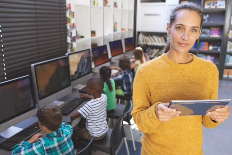 Schoolteacher looking camera and standing with tablet.